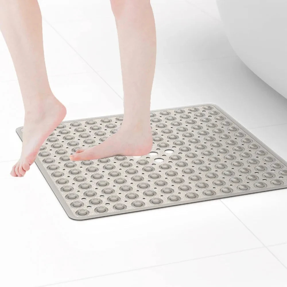 A person's bare foot is placed on a gray non-slip shower mat with suction cups for drainage.