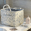 A vintage floral storage basket with a handle, featuring a light cream and blue patterned fabric.