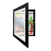 A black magnetic art frame with a glass panel displaying a watercolor scene of a sailboat on the water.