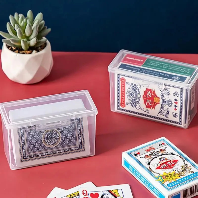 A collection of transparent plastic storage boxes for cards and sundries placed on a red surface next to a succulent plant.
