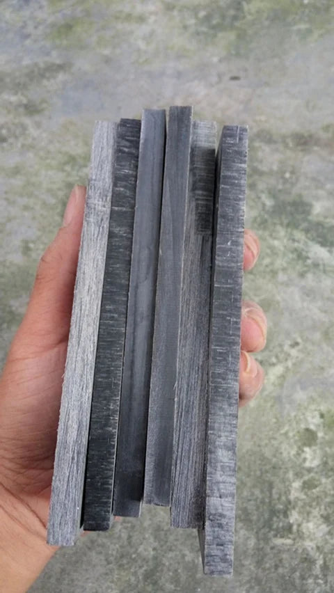 A hand holds a stack of natural buffalo horn knife handles, showing various shades of gray and black wood grain.