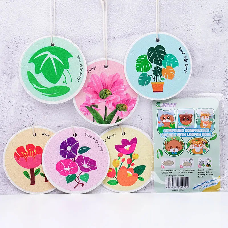 A collection of five eco-friendly wood pulp sponges in various shades of green and pink hanging on white strings.