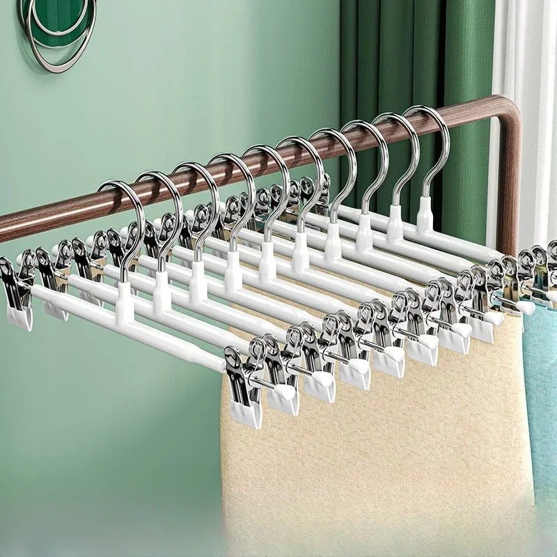 A display of stainless steel adjustable clothing hangers on a wooden rod against a light green wall.