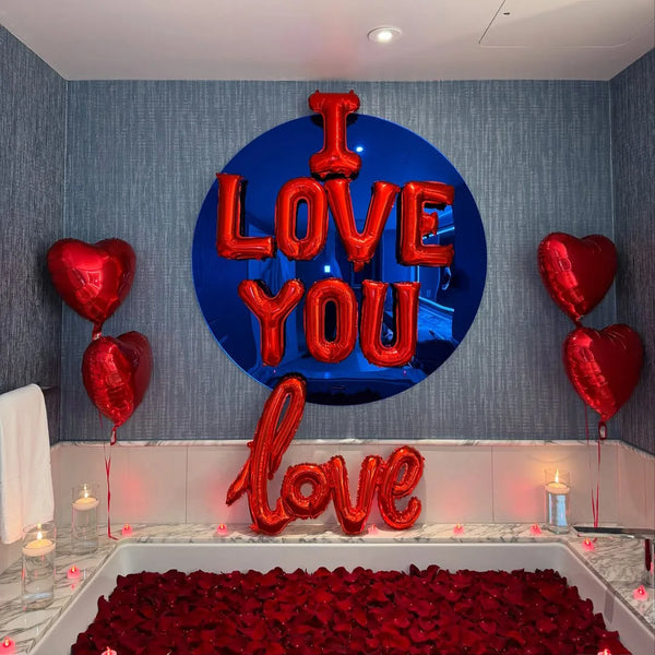Eine Anzeige mit roten Folienballons, die „I love you“ und „love“ buchstabieren, auf einer Theke mit einem Bett aus roten Ros