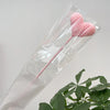 Une fleur en forme de cœur tricotée rose est présentée dans un emballage plastique transparent.