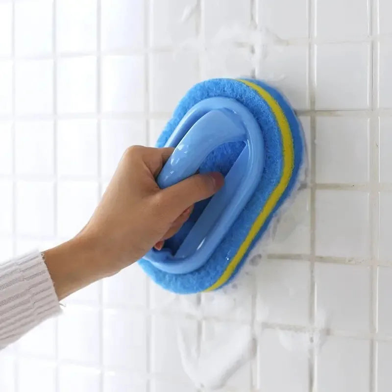 A hand is holding a blue and yellow multi-surface cleaning sponge against a white tiled wall.