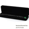 A black velvet box containing a silver necklace or bracelet with a green gemstone.