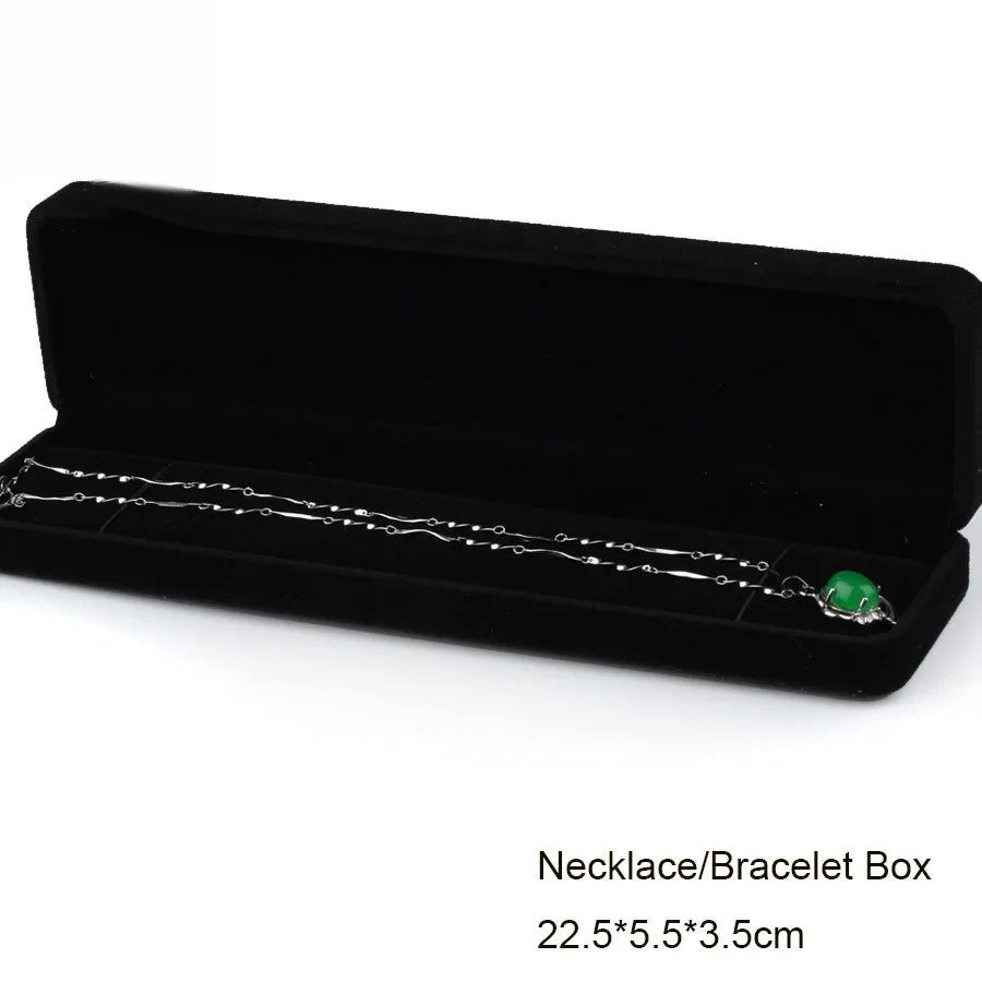 A black velvet box containing a silver necklace or bracelet with a green gemstone.