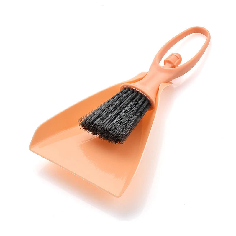 An orange mini broom and dustpan set with a handle and bristles for cleaning desks and keyboards.