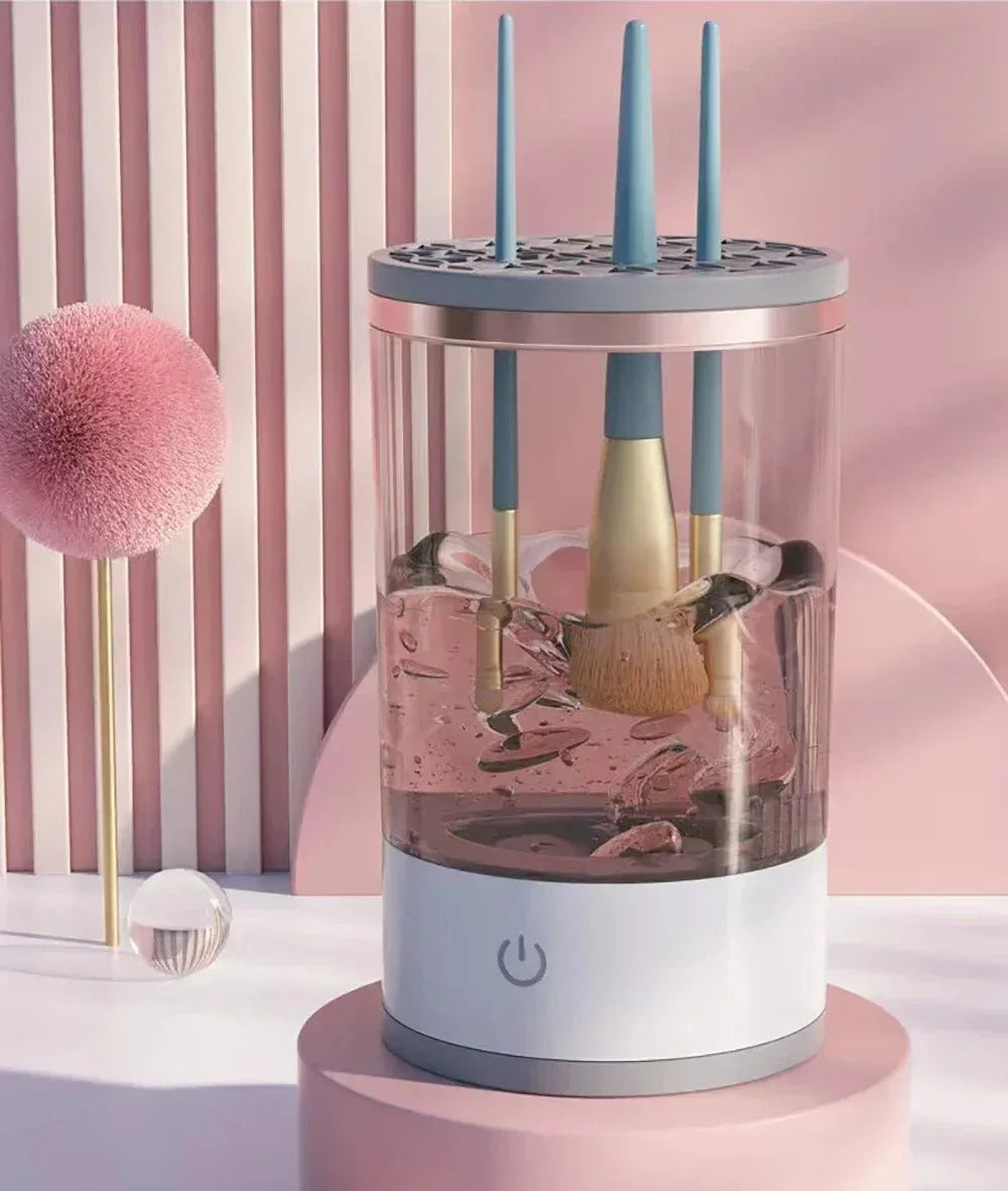 A clear glass container holds a pink liquid with makeup brushes submerged, topped by a white base and three blue cleaning too