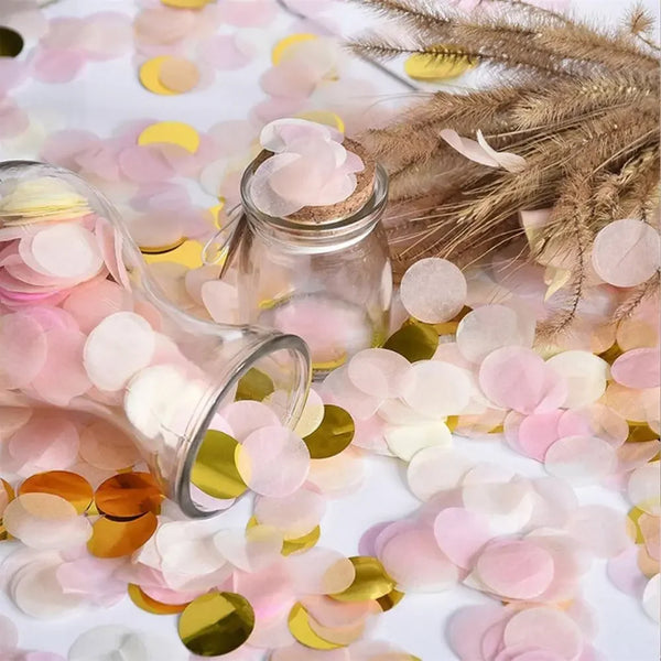 Pink and gold tissue paper confetti scattered on a white surface next to a glass jar