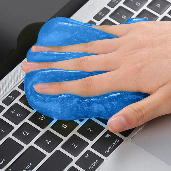 A hand is applying a bright blue, thick gel to a laptop keyboard for cleaning dust and debris.