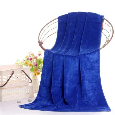 A vibrant royal blue velvet bath towel draped elegantly, with a wooden hanger and flowers in the background.
