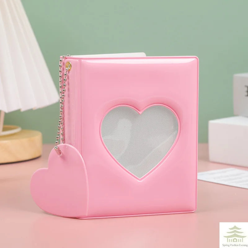A pink heart-shaped mini photo album with a clear window and a silver chain detail sits on a light surface.