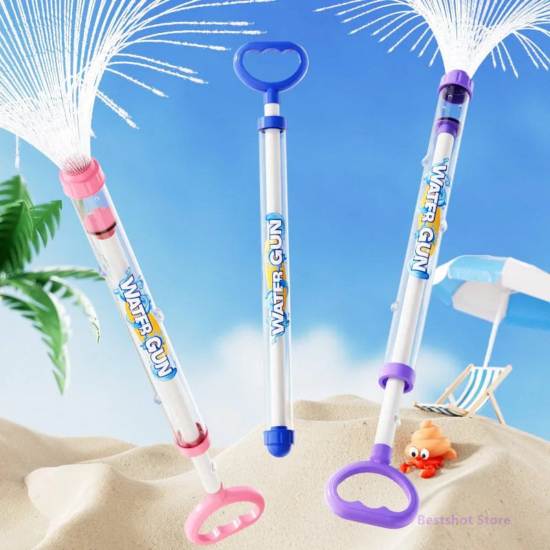 A set of pink and purple water guns with spray nozzles is shown against a blue sky on sand.