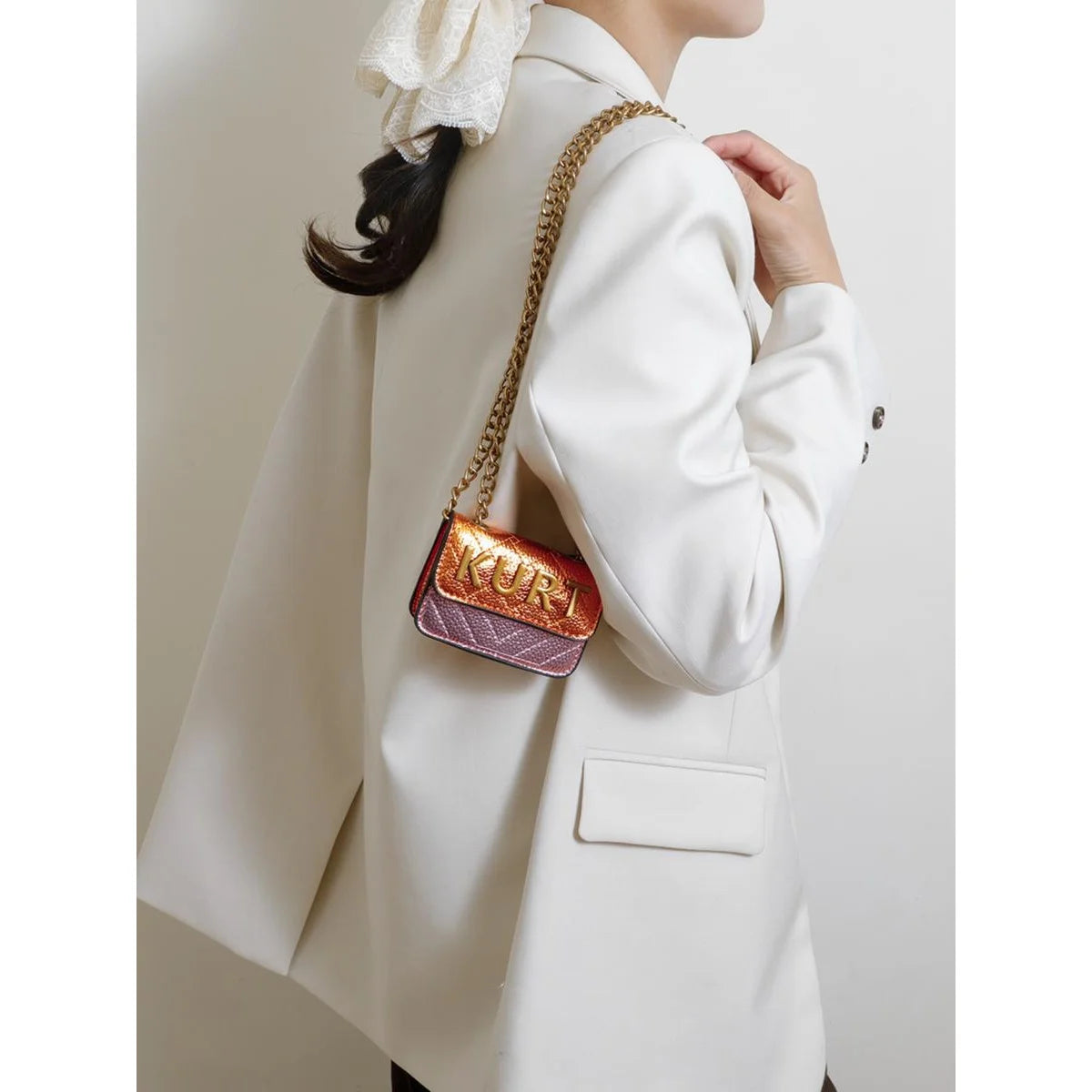 A close-up of a white blazer with a gold chain strap and a pink patterned magnetic crossbody bag.