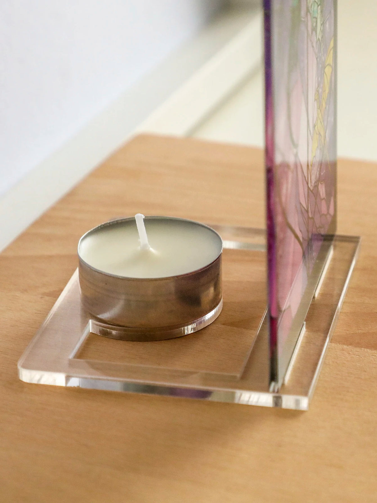 Un portavelas de plata con una vela blanca sobre una base de acrílico transparente junto a un vaso de exhibición alto.