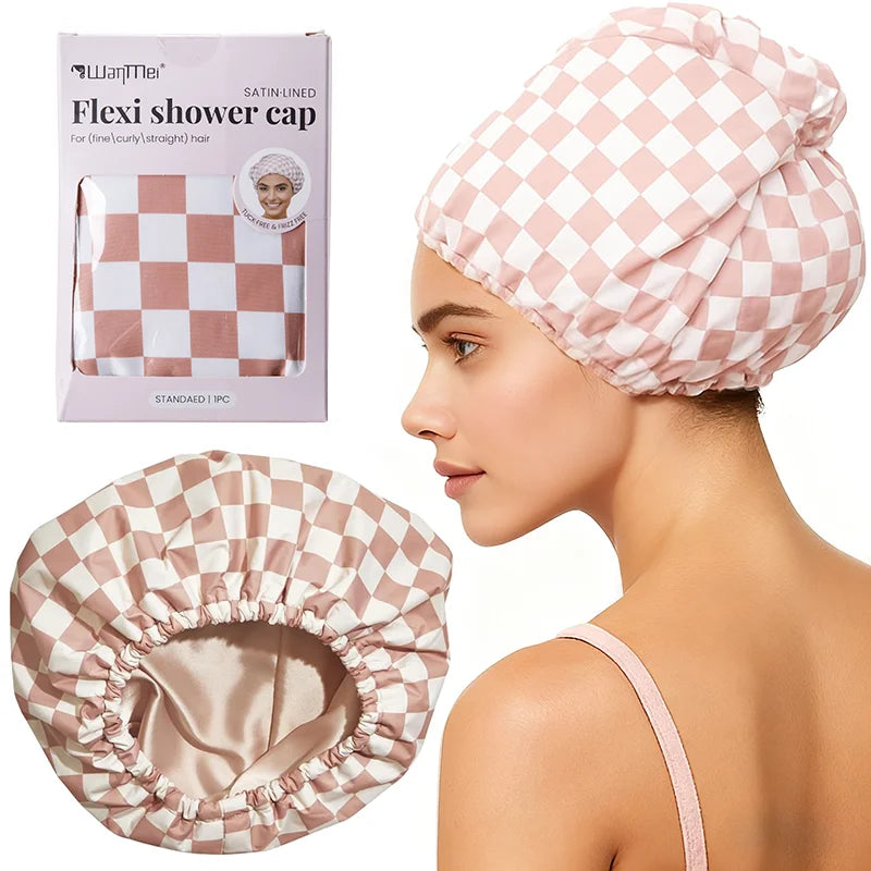 A woman is wearing a pink checkered satin-lined shower cap, with the product packaging and an unrolled cap shown nearby.