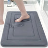 A gray non-slip absorbent bath mat is placed on a white floor, with a bare foot resting on the mat.