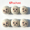 Six round, light beige wool dryer balls with small black facial features.