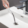 A hand is using a flexible drain cleaning brush to clear a sink drain.