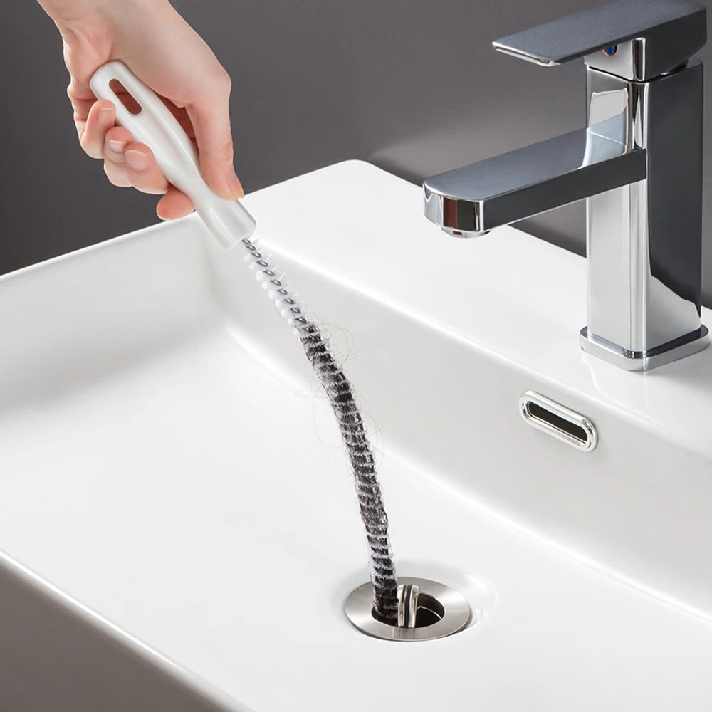 A hand is using a flexible drain cleaning brush to clear a sink drain.
