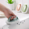 A hand is holding a green magic sponge scrubber with an ergonomic handle over a white sink.