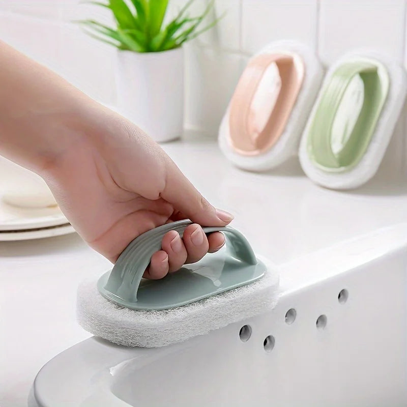 A hand is holding a green magic sponge scrubber with an ergonomic handle over a white sink.