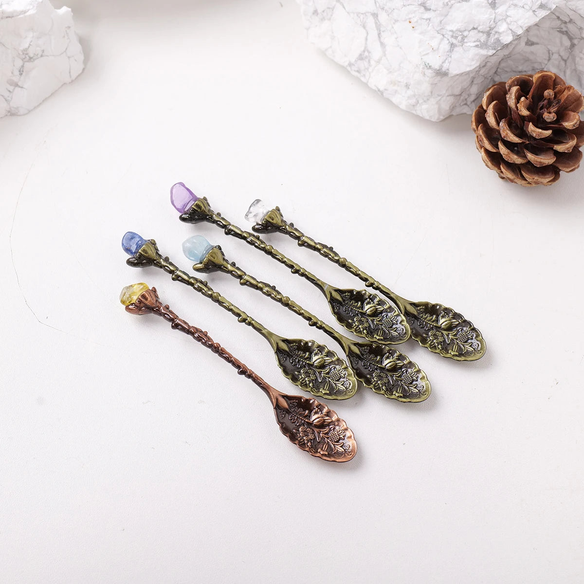 A set of natural crystal spoons with purple and blue stones resting on a white surface.