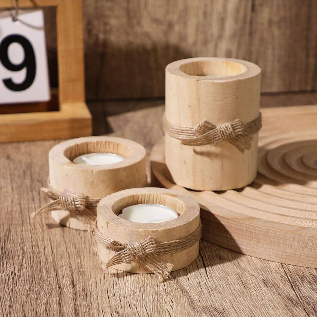 Tres portavelas cilíndricos de madera natural atados con cuerda sobre una superficie de madera.