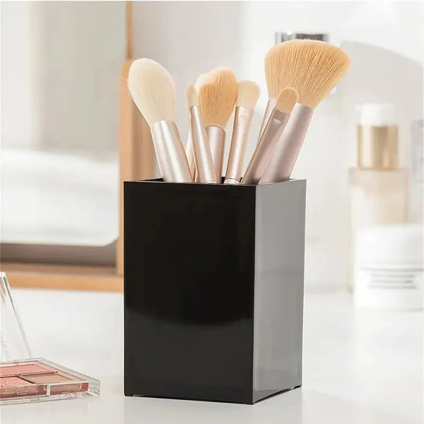 A black cosmetic storage organizer holds several makeup brushes with light beige and gold handles on a white surface.