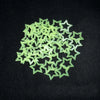 A pile of light green glow in the dark 3D star wall decals scattered on a black surface.