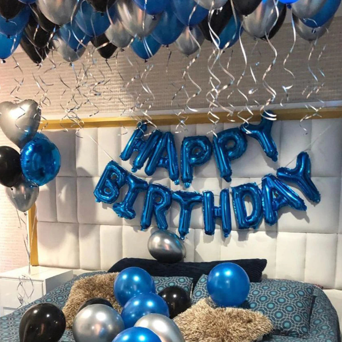 A silver and blue balloon decoration spelling out Happy Birthday on a white wall.