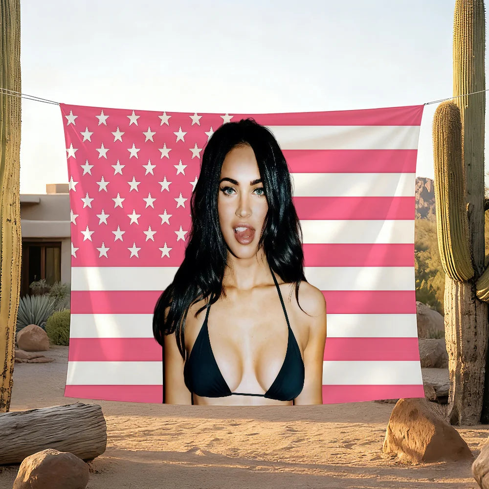 A woman posing in front of a large American flag banner with pink and white stripes and stars in a desert landscape.