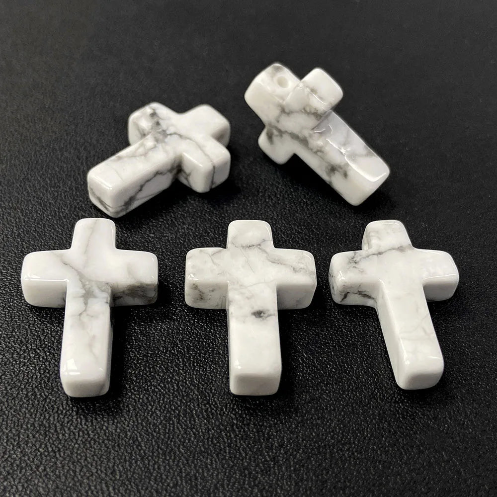 Three white marble cross pendants with grey veining displayed on a dark surface.