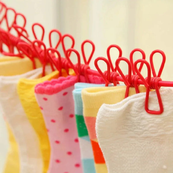 A close-up of a red retractable clothesline drying rack with colorful plastic clips holding white and yellow garments.