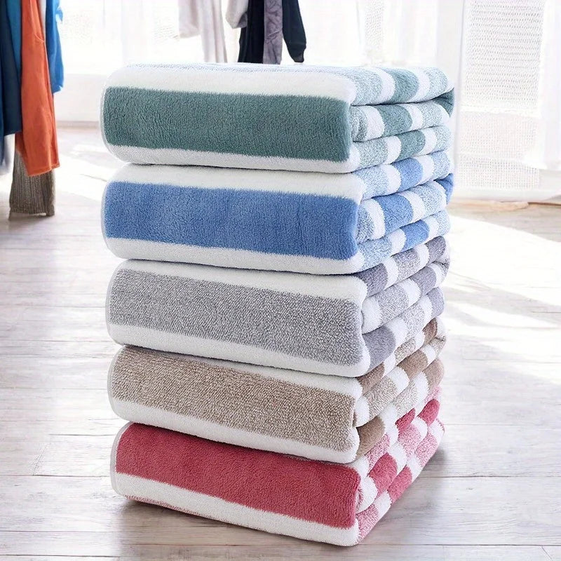 A stack of striped microfiber bath towels in various shades of blue, gray, and pink on a wooden floor.