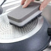 A hand places a gray cleaning sponge onto a silver kitchen appliance surface.