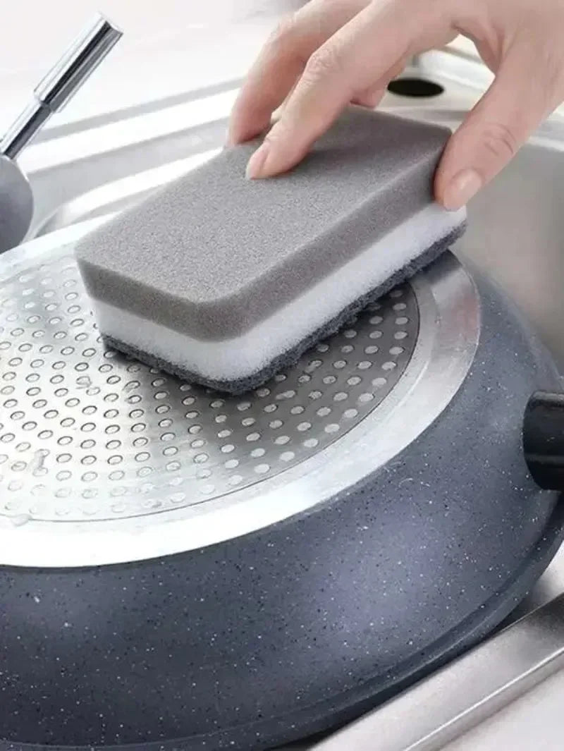 A hand places a gray cleaning sponge onto a silver kitchen appliance surface.