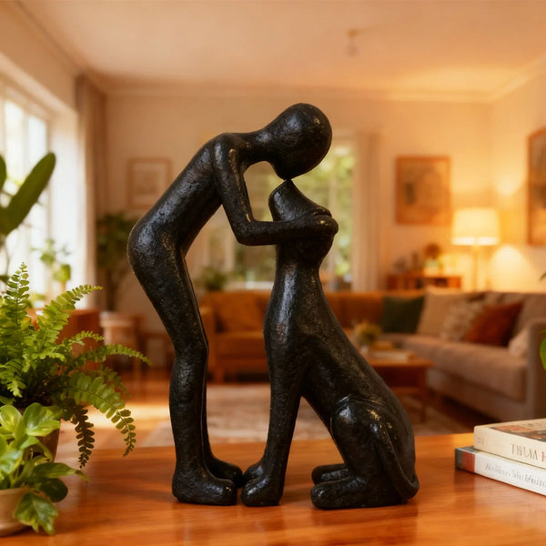 A dark resin figurine depicting a person kissing a puppy sitting on a wooden table.