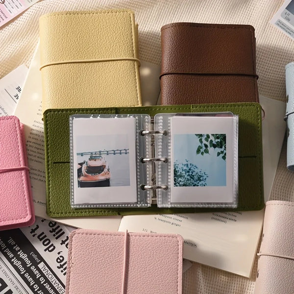 Une pile d'albums photo miniatures en similicuir vert olive et beige posés sur du papier blanc.