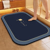 A dark blue diatomite bath mat with a gold border placed on a tiled floor.