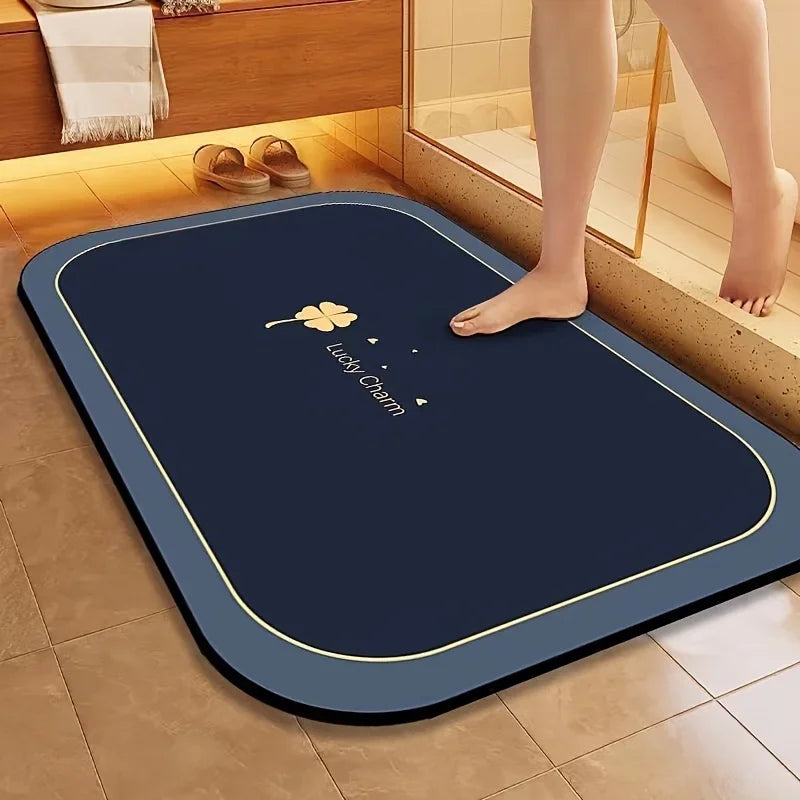 A dark blue diatomite bath mat with a gold border placed on a tiled floor.
