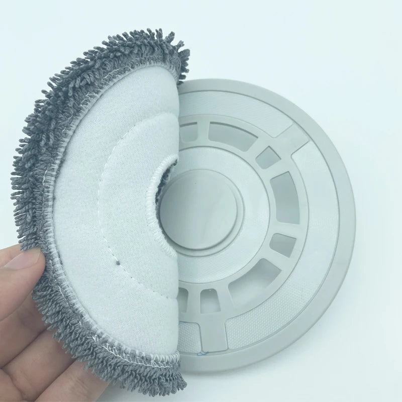 A hand holds a replacement part for a Dreame robot vacuum, showing a gray brush and a circular cleaning pad.