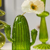 Un vase en verre cactus vert vif avec une fleur blanche est exposé sur une surface.