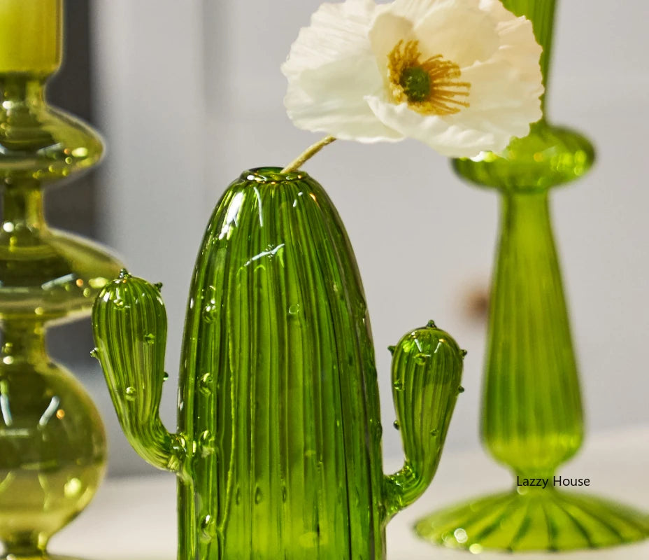 Un vase en verre cactus vert vif avec une fleur blanche est exposé sur une surface.