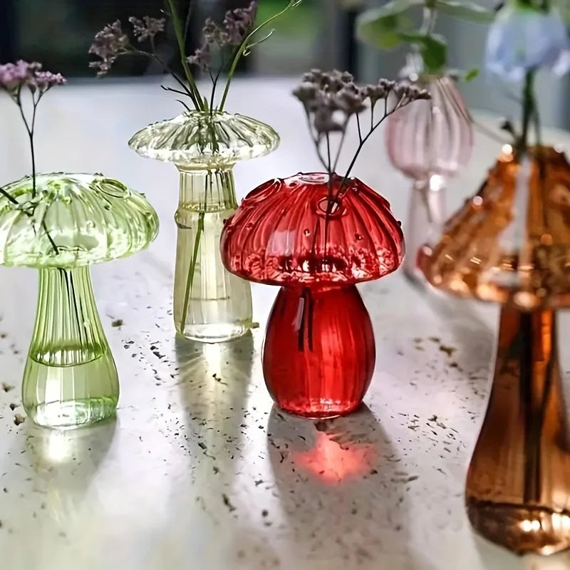 A collection of glass mushroom-shaped vases in various shades of green, pink, and amber on a reflective surface.