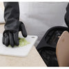 A hand wearing a black rubber cleaning glove is handling chopped celery on a white cutting board.
