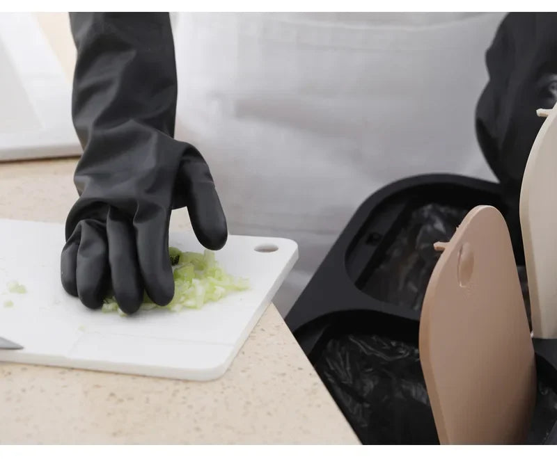 A hand wearing a black rubber cleaning glove is handling chopped celery on a white cutting board.