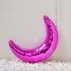 A pink, iridescent mosaic moon pendant hanging against a white background on a bed of white pebbles.